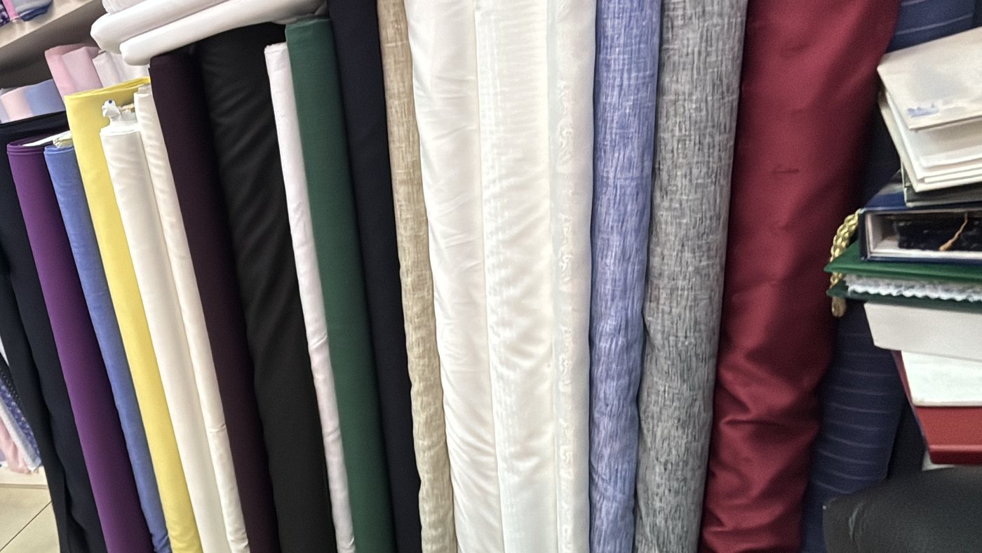 Shelves of suiting and shirting cloth in navy, grey, green, purple, cream and burgundy