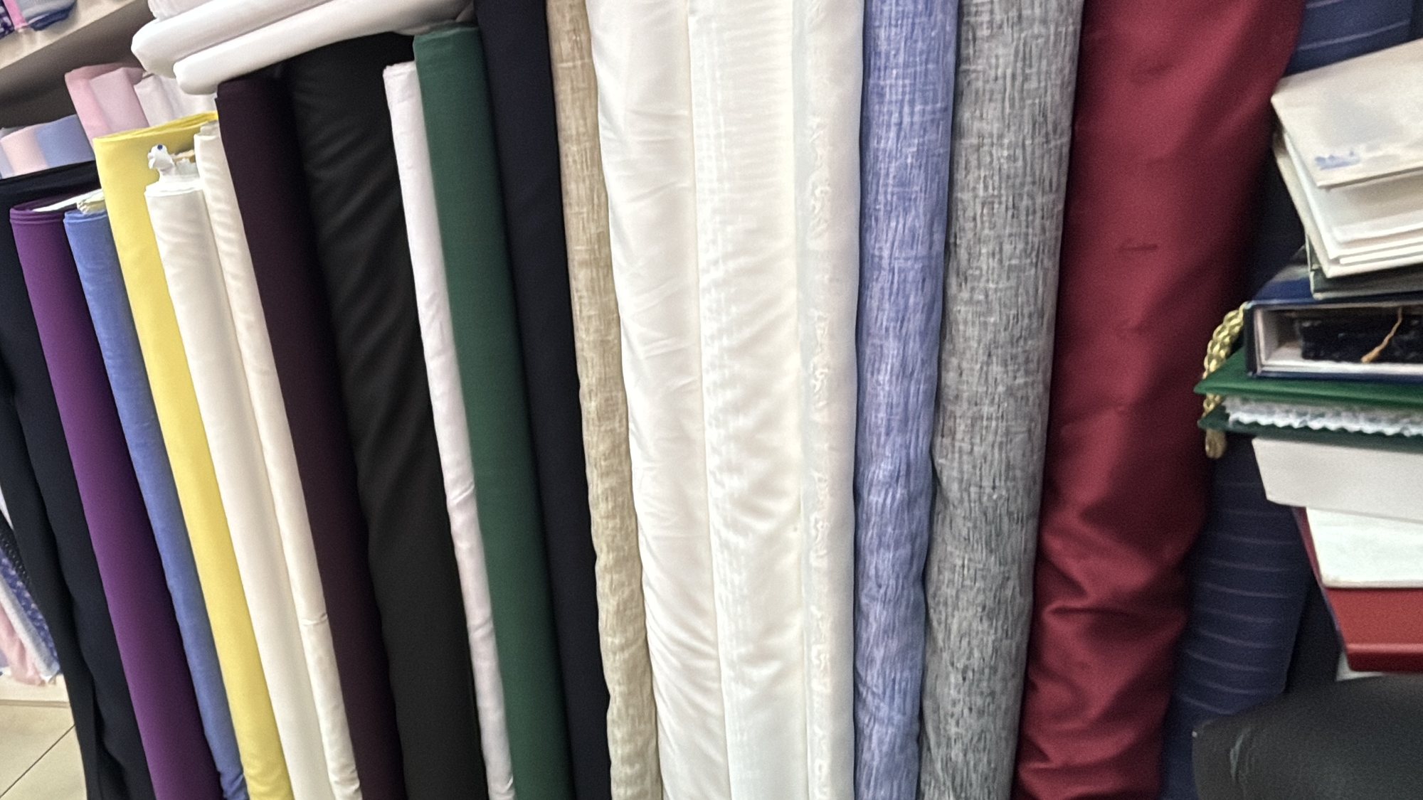 Shelves of suiting and shirting cloth in the shop, in navy, grey, green, purple, cream and burgundy