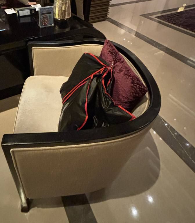 A finished garment in a black and red garment bag, left on an armchair in a hotel lobby