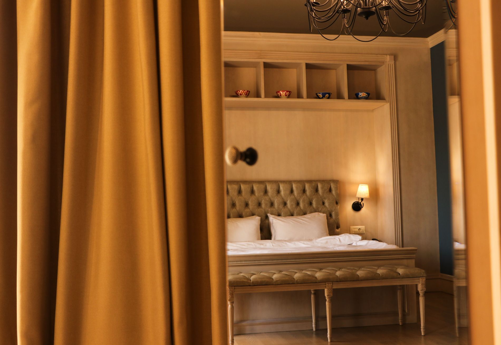 A warmly lit hotel room seen past a heavy gold curtain