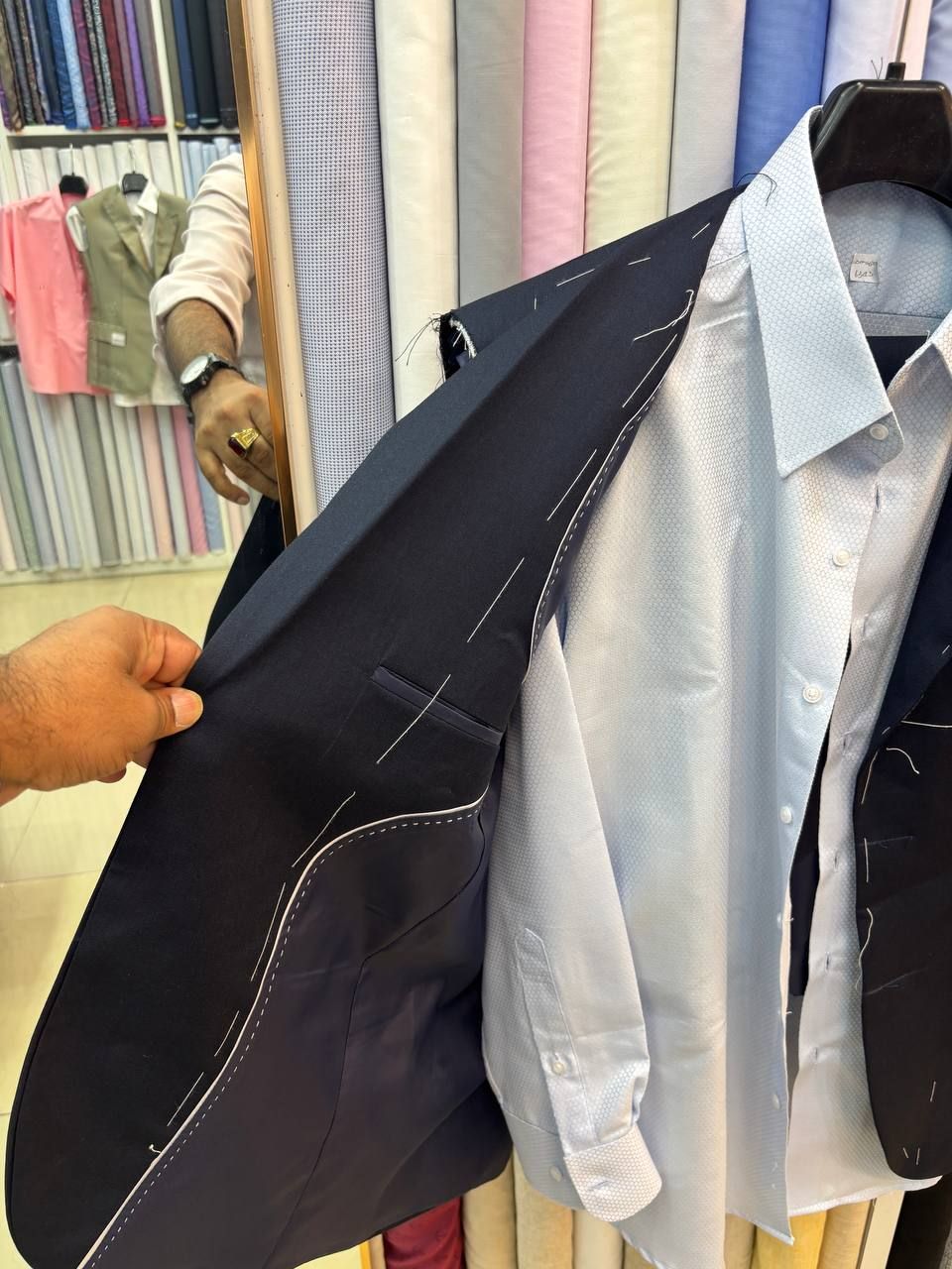 A dark jacket with white basting stitches still in, shown with a pale blue shirt in the shop