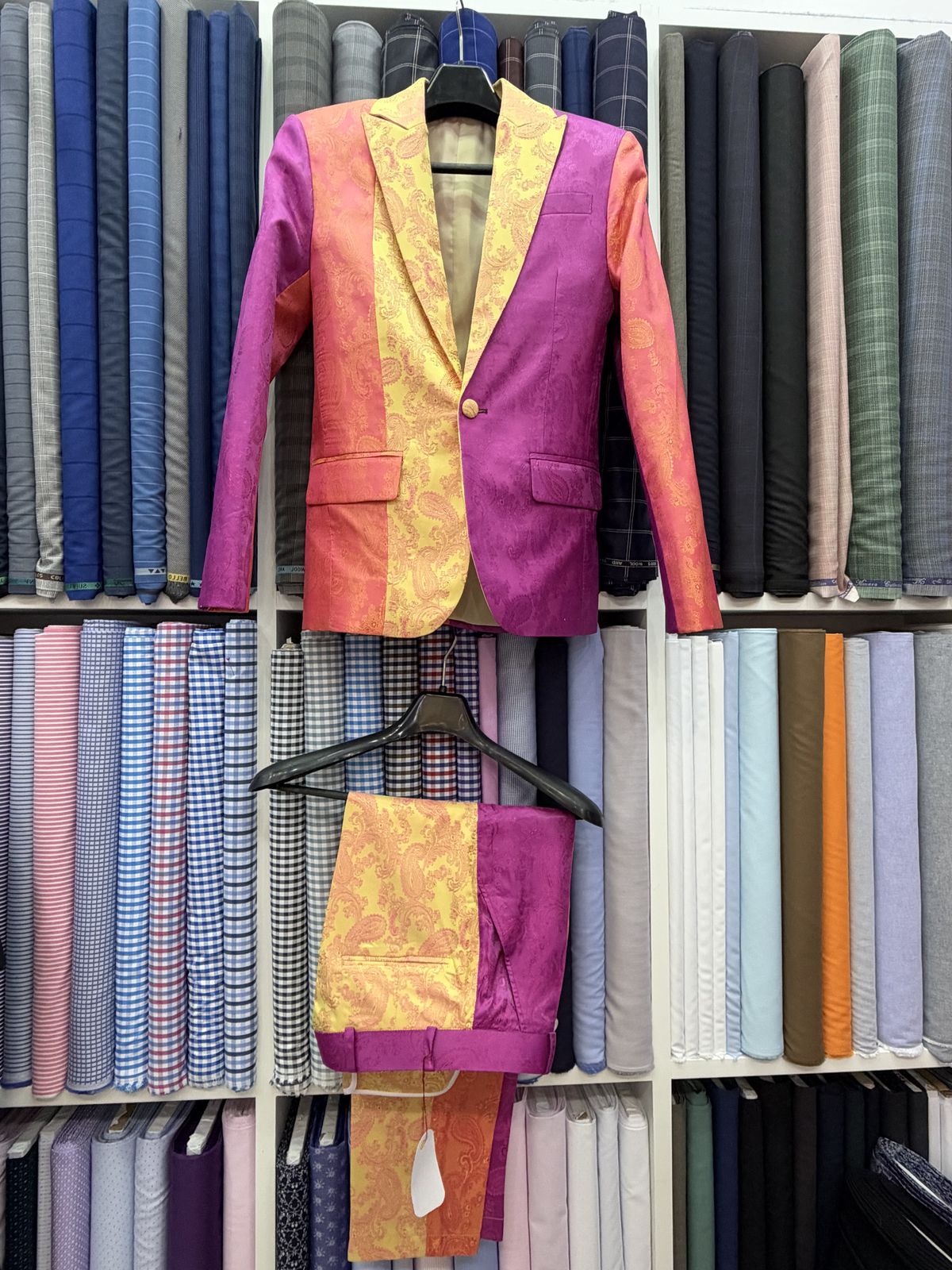 Pink, orange and gold paisley occasion jacket with matching trousers hanging in the shop