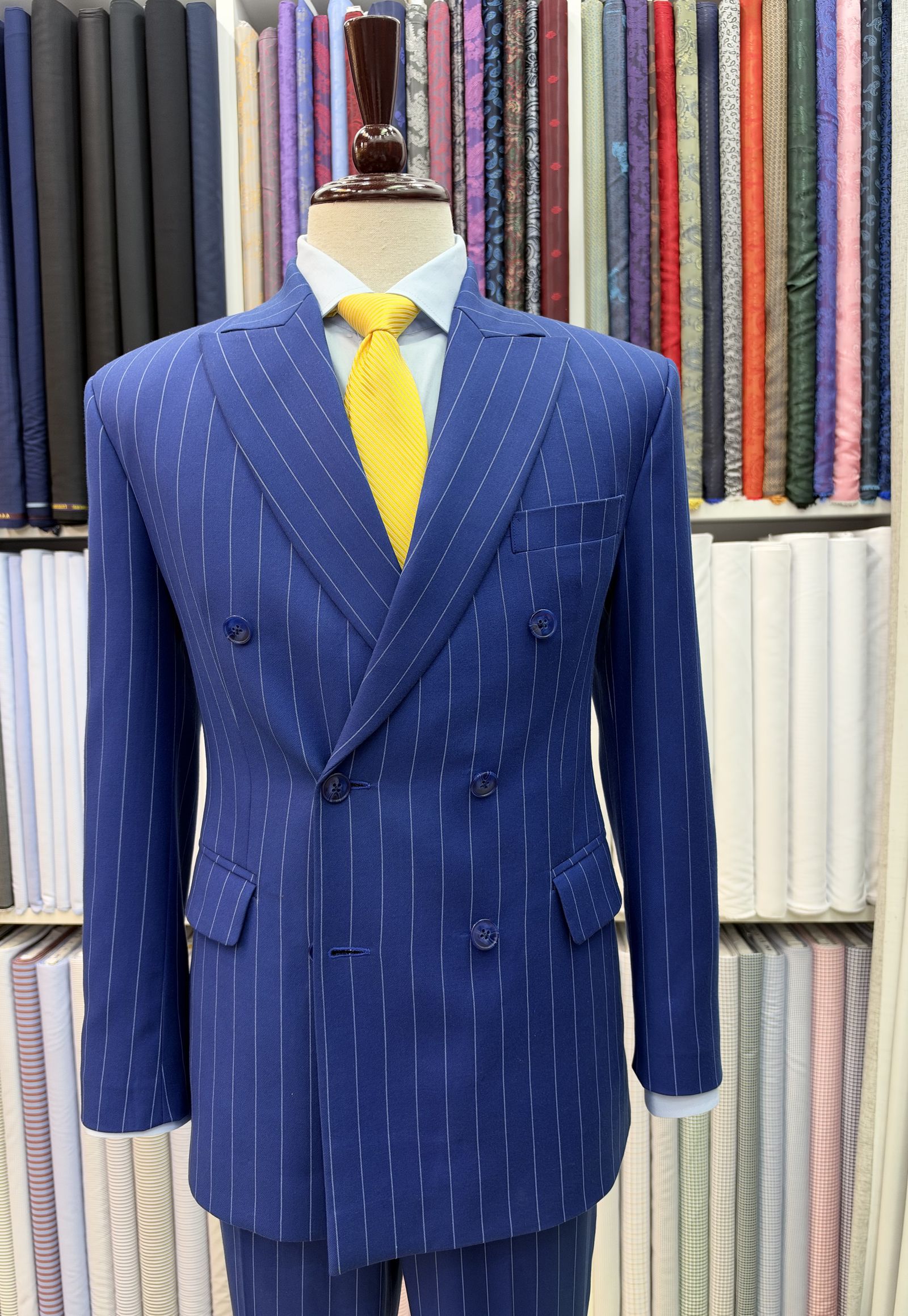 Bright blue double-breasted chalk-stripe suit with peak lapels and a yellow tie on a stand