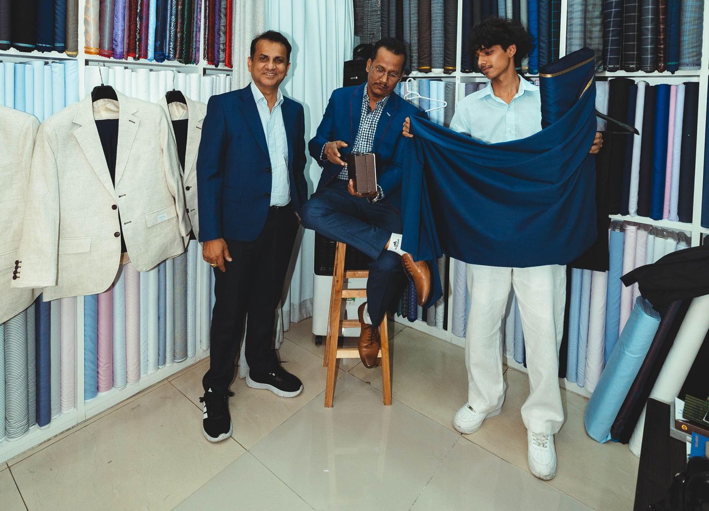 Staff in the shop, one holding up a length of navy cloth, in front of shelves of fabric