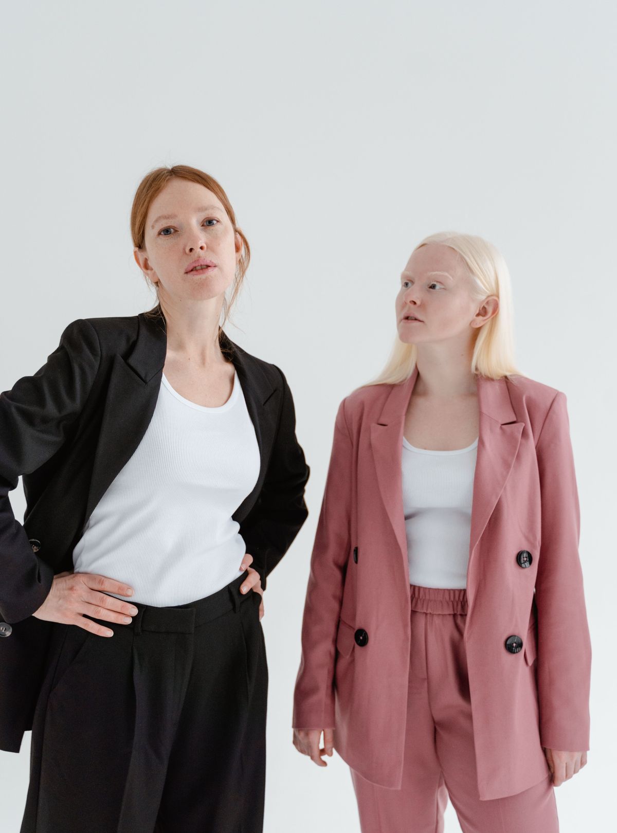Two women in tailored trouser suits, one black, one dusty pink double-breasted