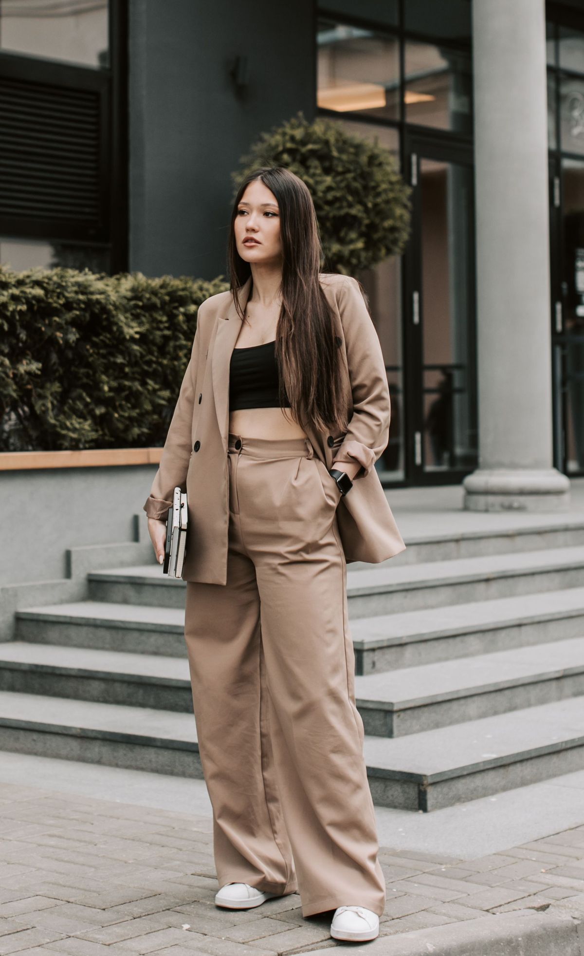 A woman in a relaxed camel trouser suit standing on city steps